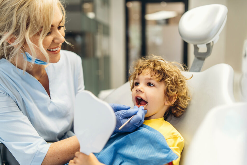 A dentist near Lenexa checking a child's teeth while he holds up a hand mirror.